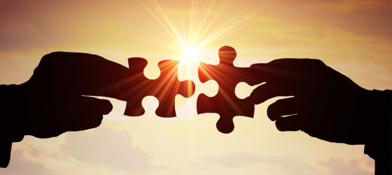 due mani al tramonto che si passano dei pezzi di un puzzle