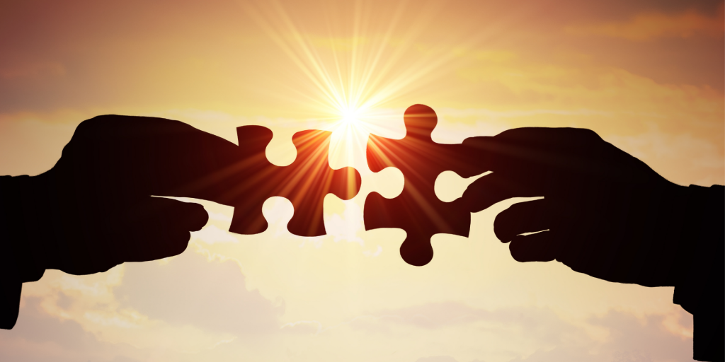 due mani al tramonto che si passano dei pezzi di un puzzle